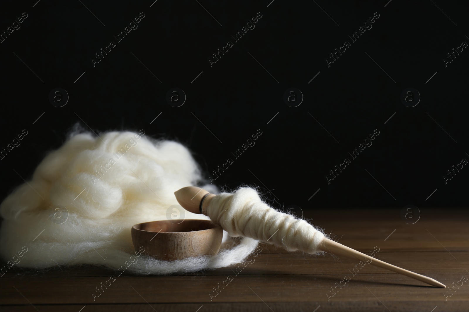 Photo of Soft white wool and spindle on wooden table against black background, space for text