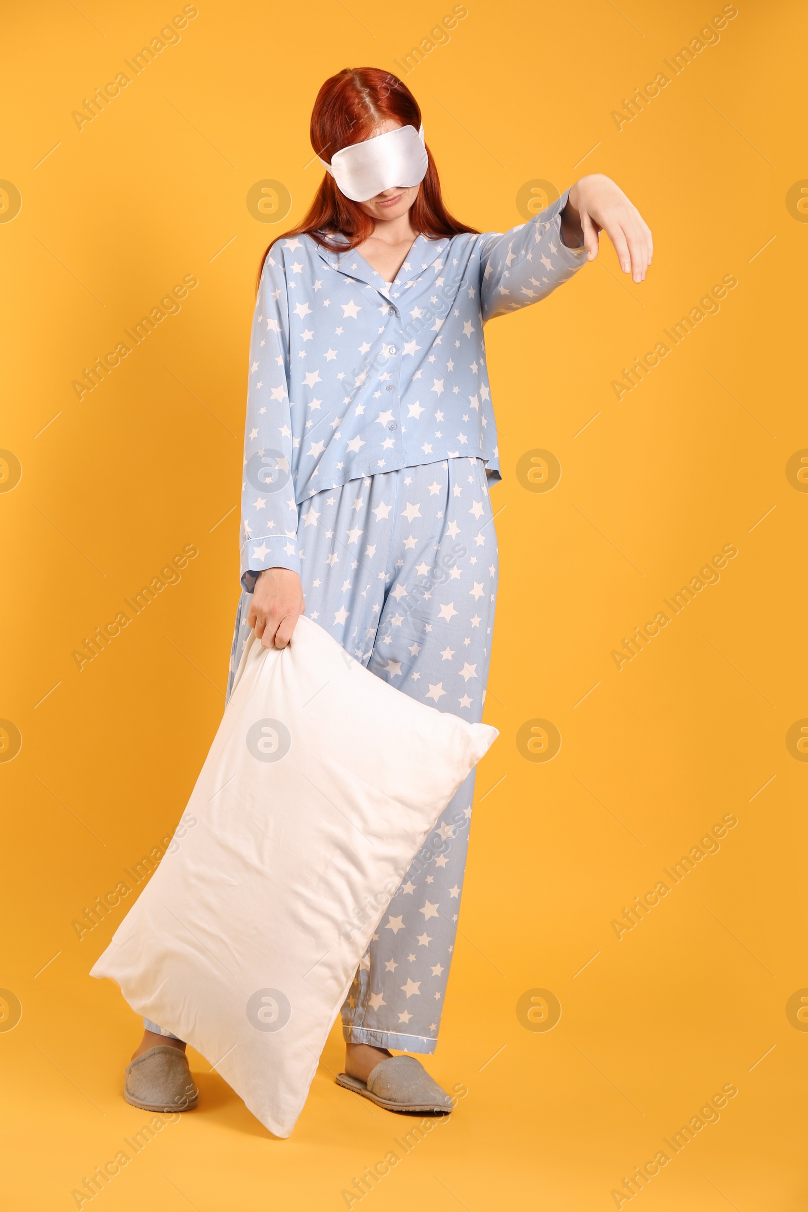 Photo of Young woman wearing pajamas and slippers with pillow in sleepwalking state on yellow background