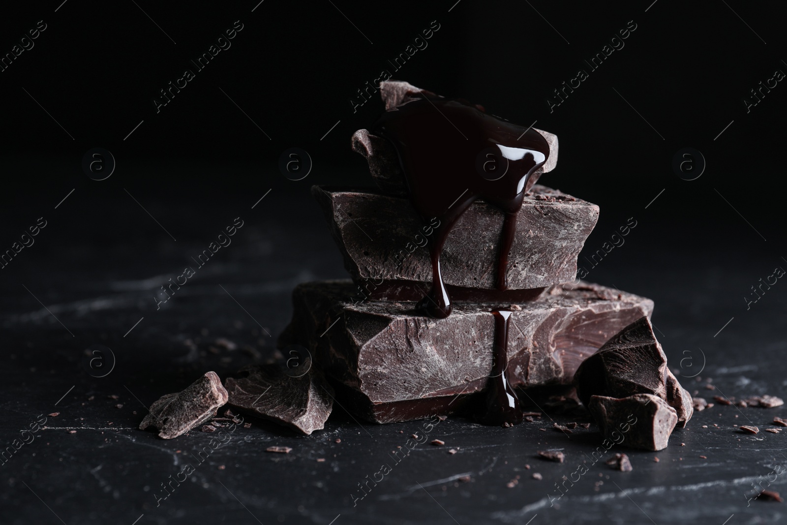 Photo of Pieces of tasty dark chocolate with syrup on black table, closeup