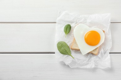 Photo of Heart shaped fried egg with toast and spinach on white wooden table, top view. Space for text