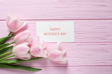 Photo of Tulips and greeting card with phrase "Happy Mother's Day" on wooden background