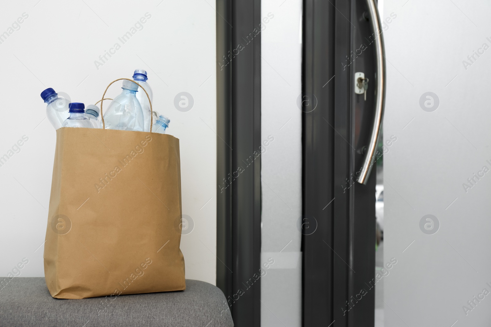 Photo of Paper bag with used plastic bottles near entrance door in hallway. Recycling problem