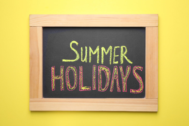 Photo of Chalkboard with phrase SUMMER HOLIDAYS on yellow background, top view. School's out
