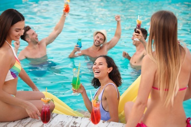 Photo of Happy young friends with refreshing cocktails enjoying pool party