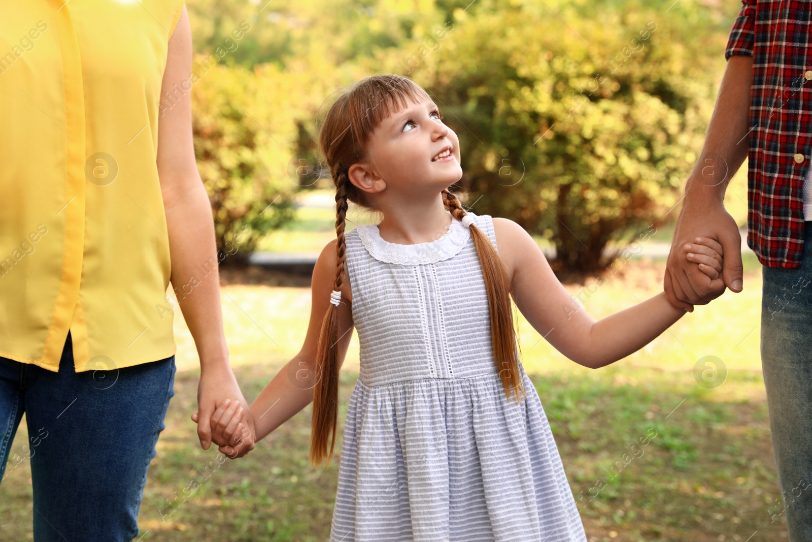 Photo of Little girl and her parents holding hands outdoors. Family weekend