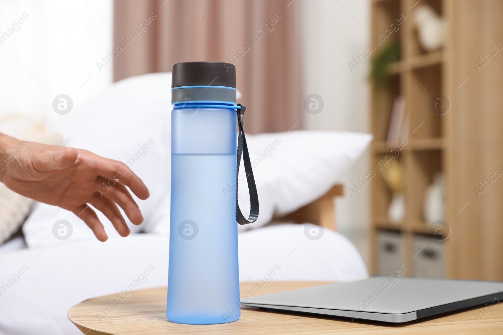 Photo of Man taking transparent plastic bottle of water from table indoors, closeup