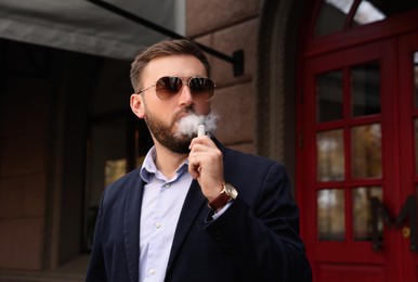 Photo of Handsome young businessman using disposable electronic cigarette outdoors
