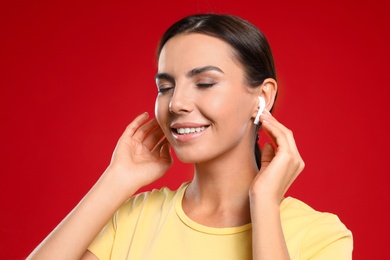 Photo of Happy young woman listening to music through wireless earphones on red background