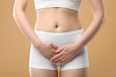 Woman suffering from cystitis on beige background, closeup