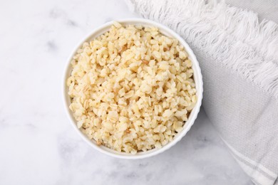 Cooked bulgur in bowl on white marble table, top view