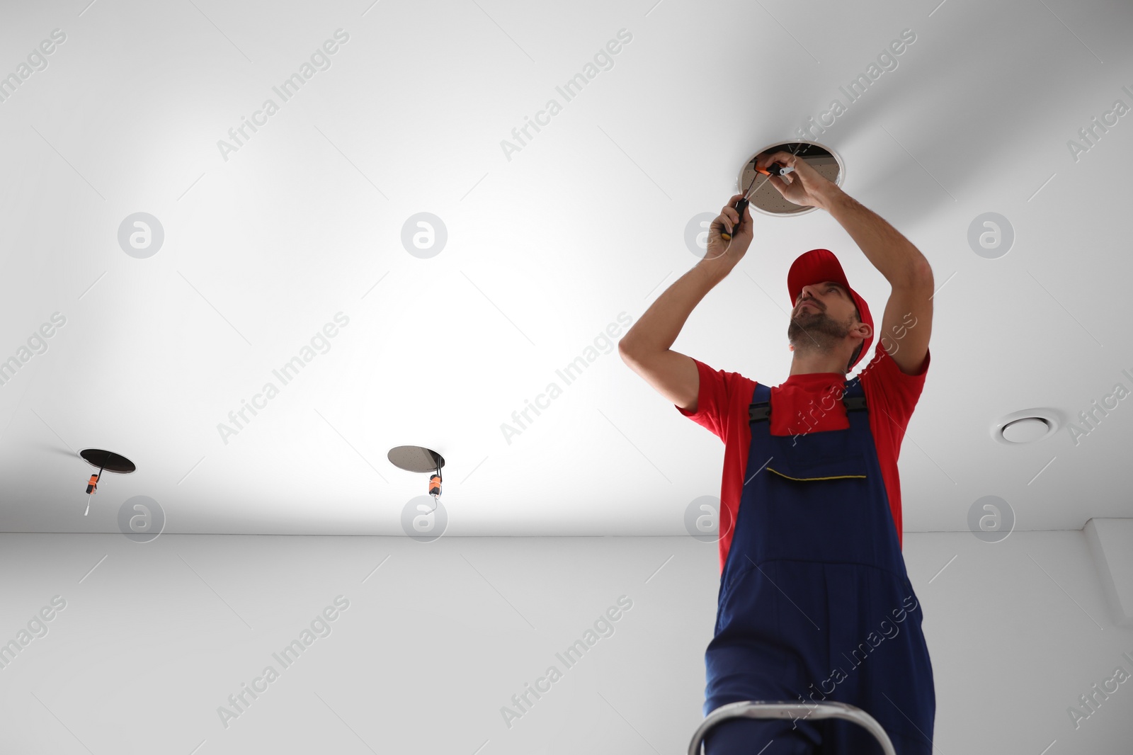 Photo of Worker installing lamp on stretch ceiling indoors. Space for text