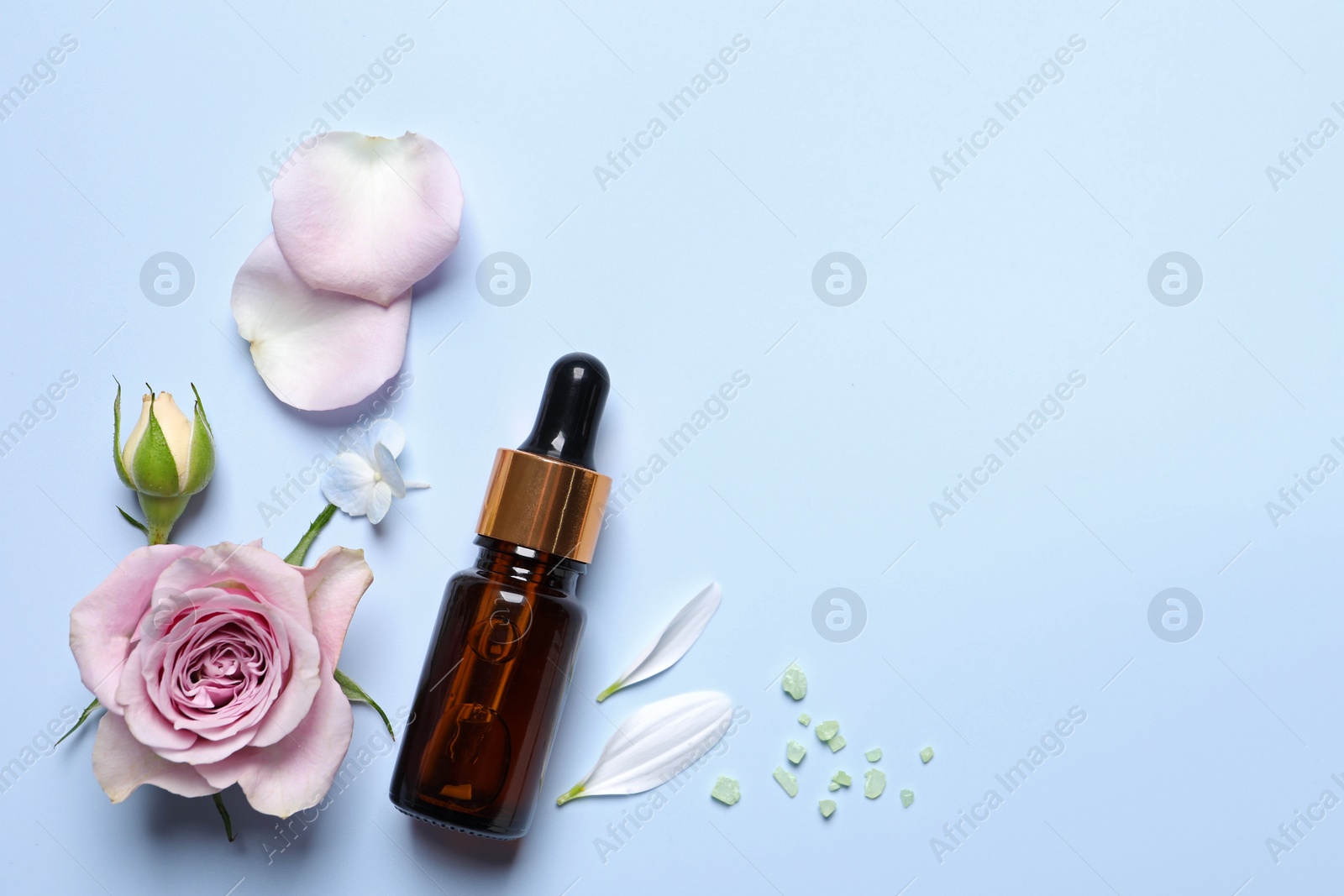 Photo of Bottle of cosmetic serum, beautiful flowers and sea salt on light blue background, flat lay