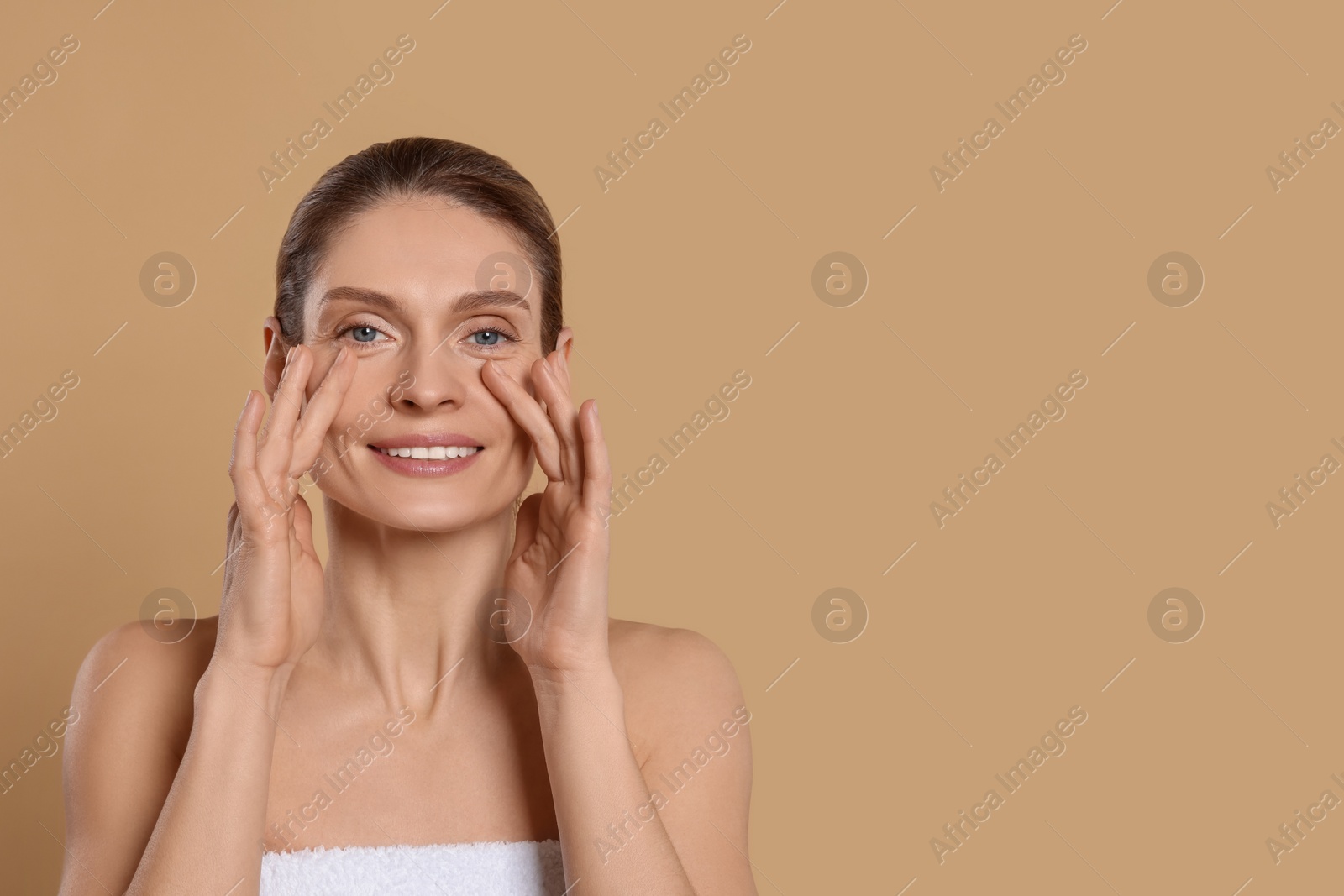 Photo of Woman massaging her face on beige background. Space for text