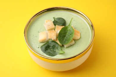 Delicious spinach cream soup with croutons in bowl on yellow background