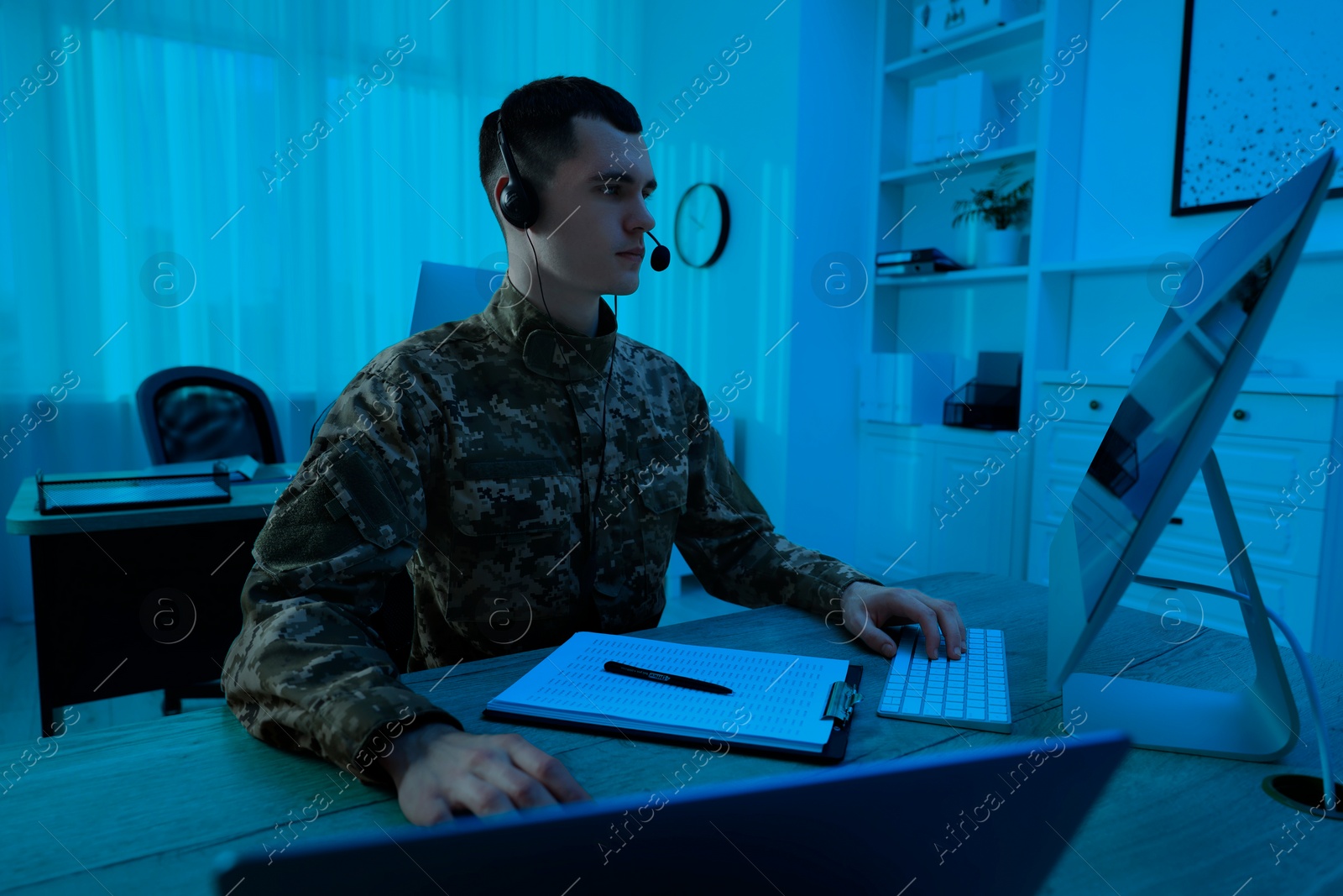 Image of Military service. Soldier in headphones working on computer at wooden table in office at night