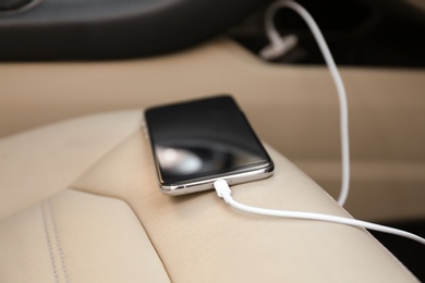 Photo of Mobile phone with charging cable in car, closeup