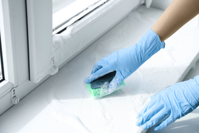 Woman cleaning window sill with sponge, closeup