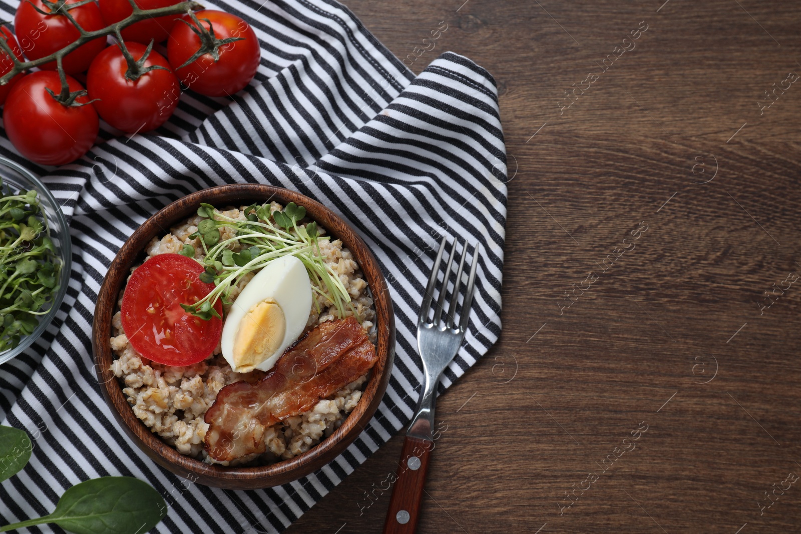 Photo of Delicious boiled oatmeal with egg, bacon and tomato served on wooden table, flat lay. Space for text