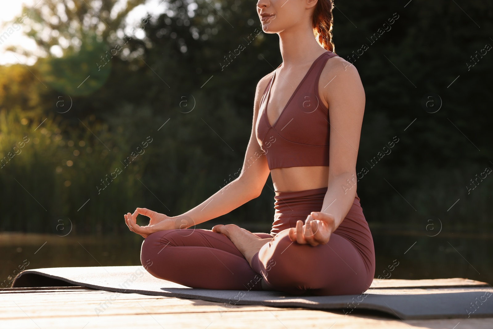 Photo of Woman practicing Padmasana on yoga mat on wooden pier near pond, closeup with space for text. Lotus pose