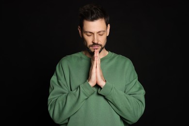 Man with clasped hands praying on black background