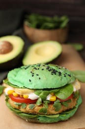 Tasty green vegan burger with vegetables, patty and microgreens on parchment, closeup