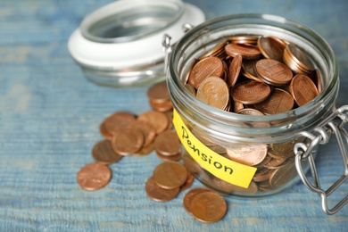Photo of Coins in glass jar with label "PENSION" on wooden table. Space for text