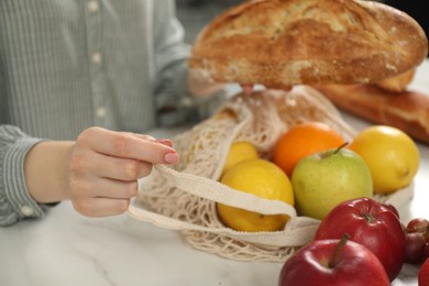 Photo of Woman with string bag of fresh fruits and bread at light marble table, closeup