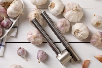 Metal press and garlic on white wooden table, flat lay