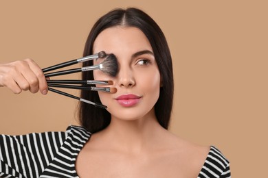 Photo of Beautiful woman with different makeup brushes on light brown background