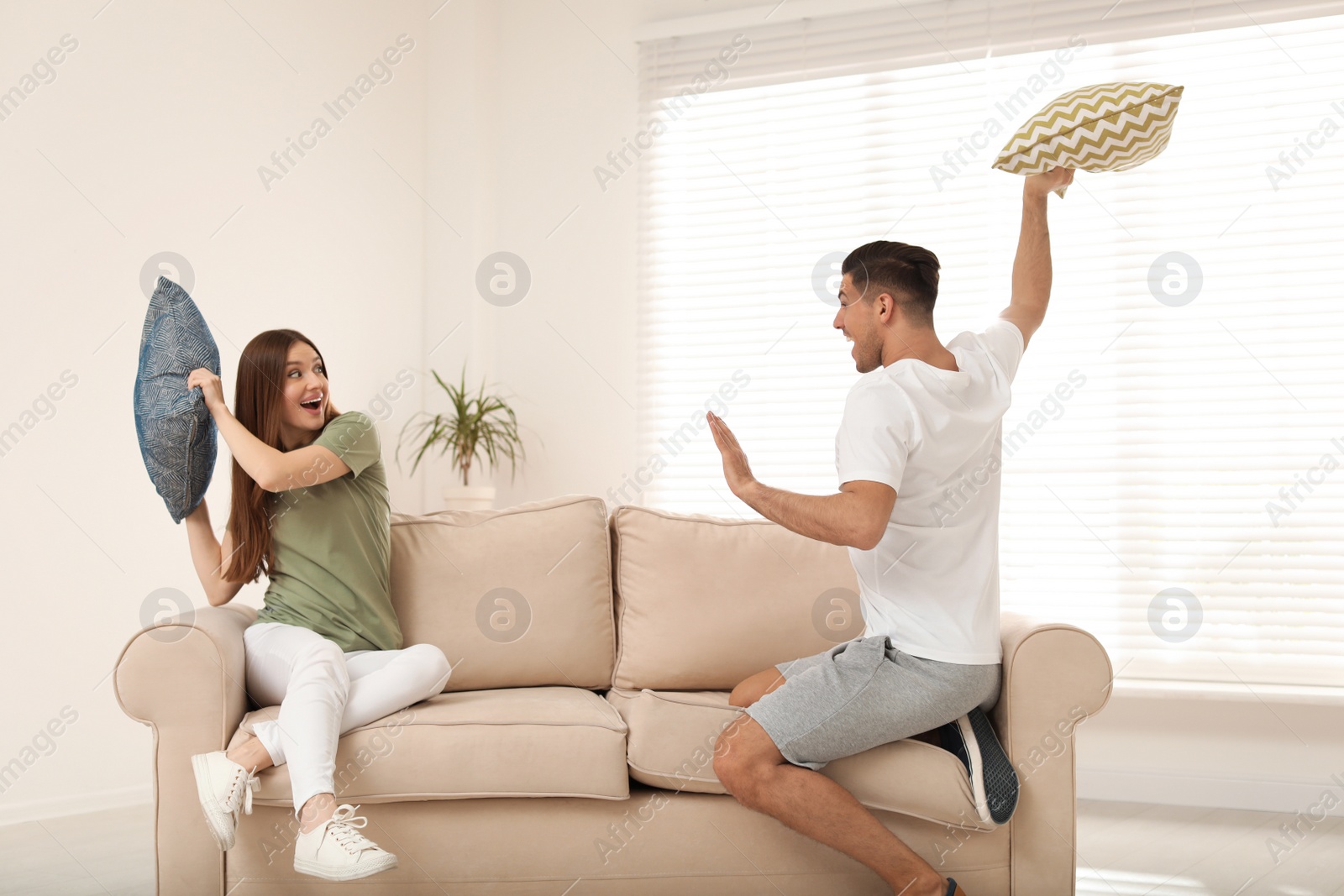 Photo of Happy couple having pillow fight in living room