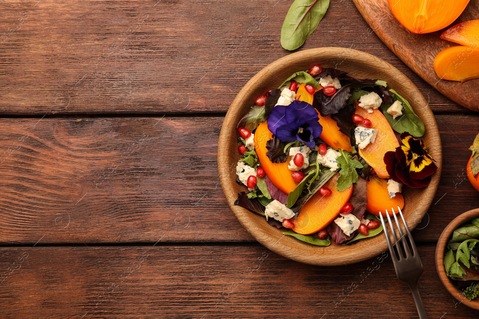 Photo of Delicious persimmon salad with cheese and pomegranate served on wooden table, flat lay. Space for text