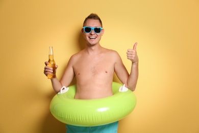 Shirtless man with inflatable ring and bottle of drink on color background