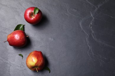 Photo of Ripe red apples and leaves on black textured table, flat lay. Space for text