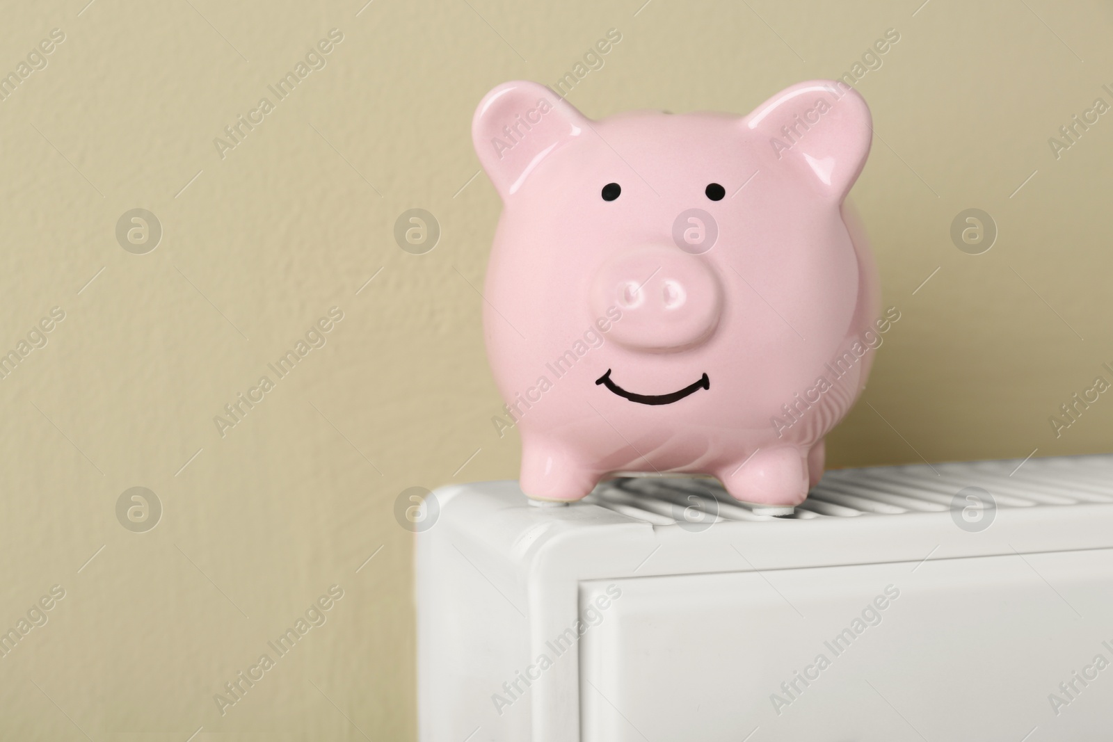 Photo of Piggy bank on heating radiator against beige background, space for text