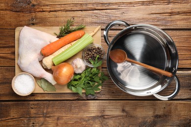 Pot with ladle and different ingredients for cooking tasty bouillon on wooden table, flat lay