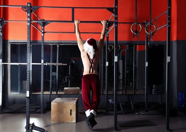 Young shirtless Santa Claus training in modern gym, back view
