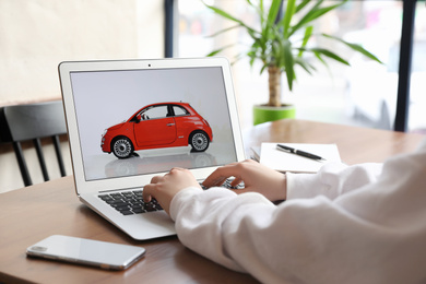 Woman using laptop to buy car at wooden table indoors, closeup