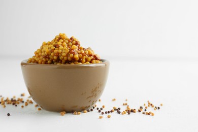 Photo of Fresh whole grain mustard in bowl and dry seeds on white table. Space for text