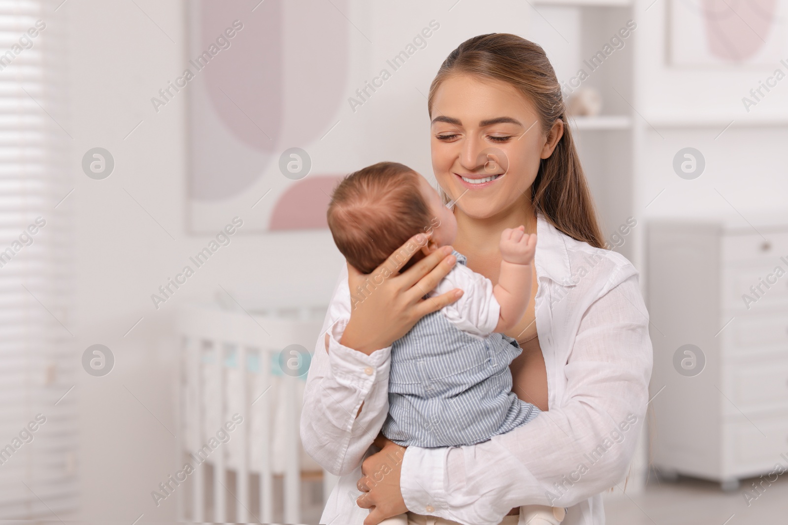 Photo of Mother holding her cute newborn baby in child's room, space for text