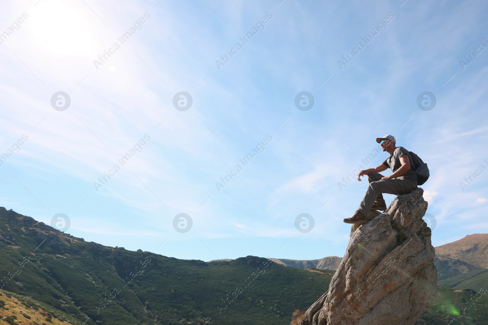 Photo of Man with backpack on rocky peak in mountains. Space for text