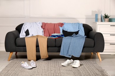 Photo of Shoes near sofa with different clothes indoors