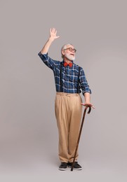 Photo of Cheerful senior man with walking cane on gray background