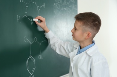 Photo of Schoolboy writing chemistry formula on blackboard in class