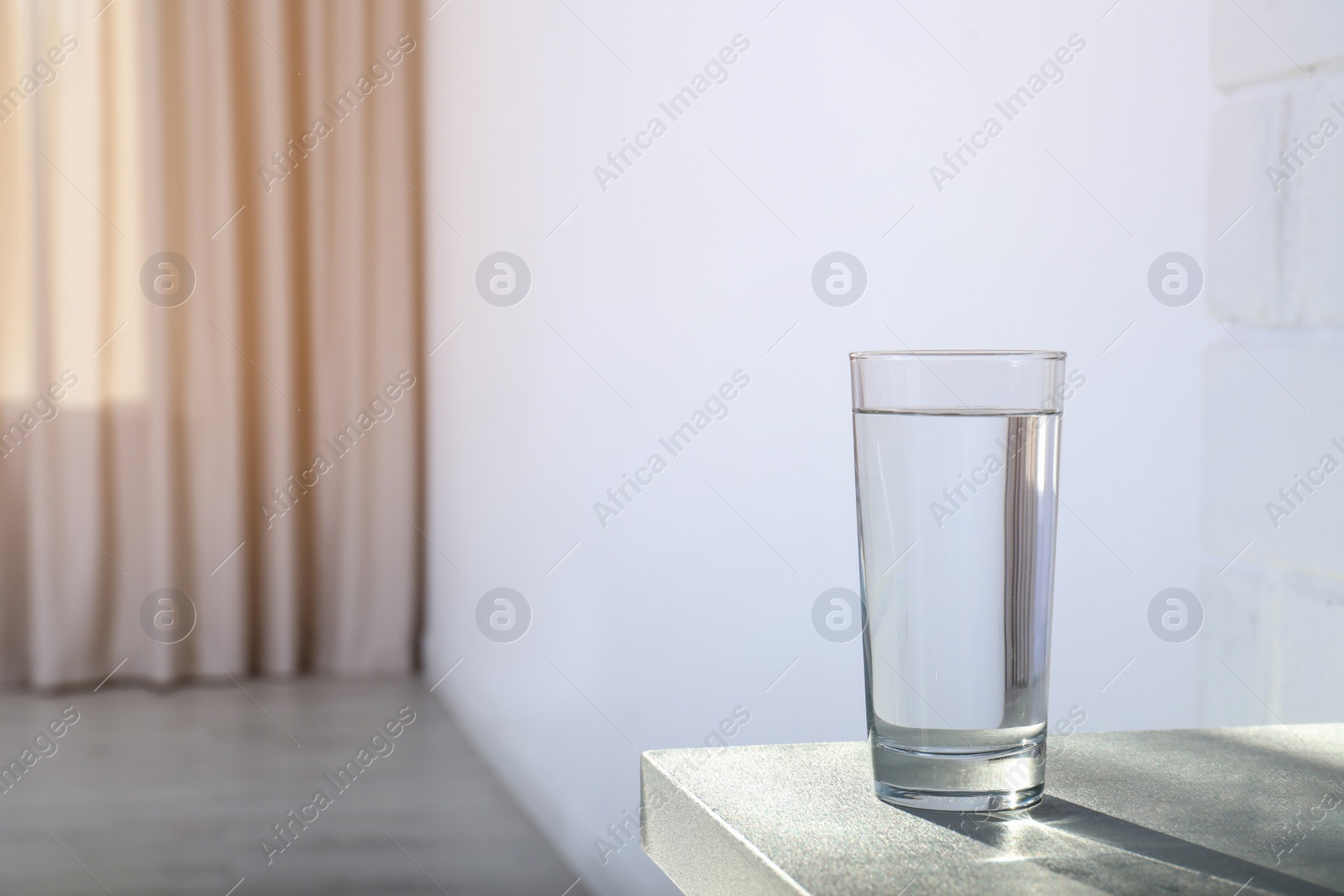 Photo of Glass of water on table against blurred background. Space for text