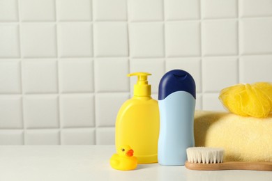 Photo of Baby cosmetic products, bath duck, brush and towel on white table against tiled wall. Space for text