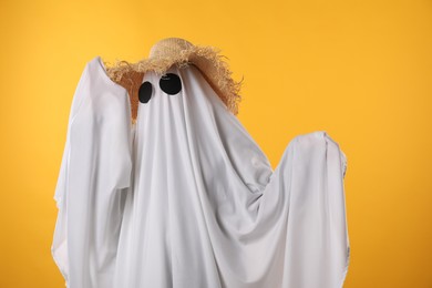 Photo of Person in ghost costume and straw hat on yellow background