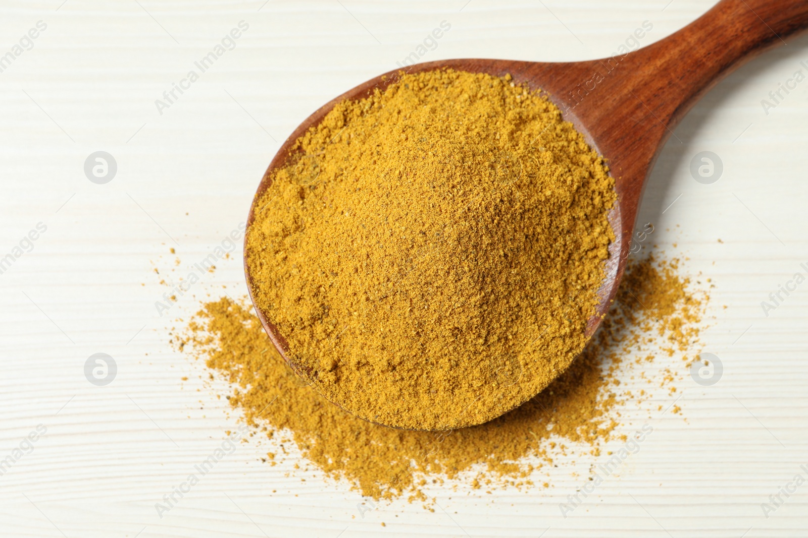 Photo of Curry powder in spoon on white wooden table, top view