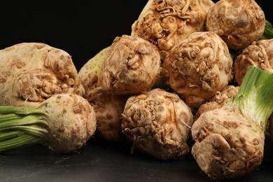 Photo of Fresh raw celery roots on black table, closeup