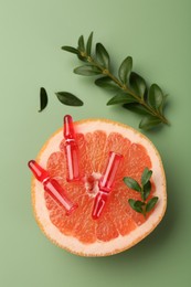 Skincare ampoules with vitamin C, half of grapefruit and leaves on light green background, flat lay