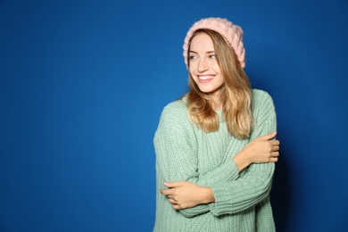 Image of Happy young woman wearing warm sweater and knitted hat on blue background
